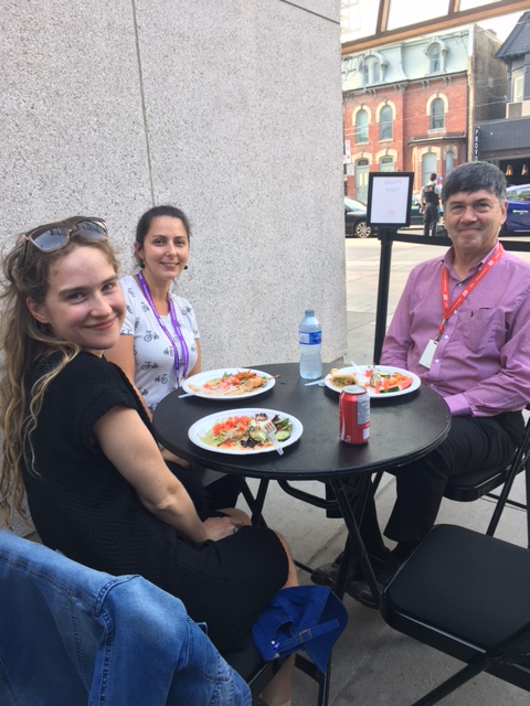 3 smiling people at a table outside in the city eating from plates of BBQ