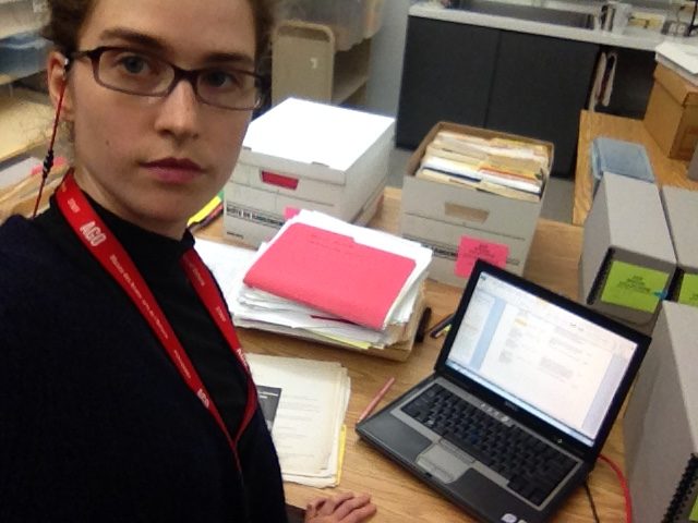 archivist with glasses in a room surrounded by latptop and boxes of papers